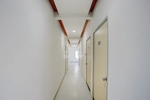 A long, narrow hallway with doors on one side and a plain wall on the other. - Collection O Warje Pune Formerly Choice (Pune)