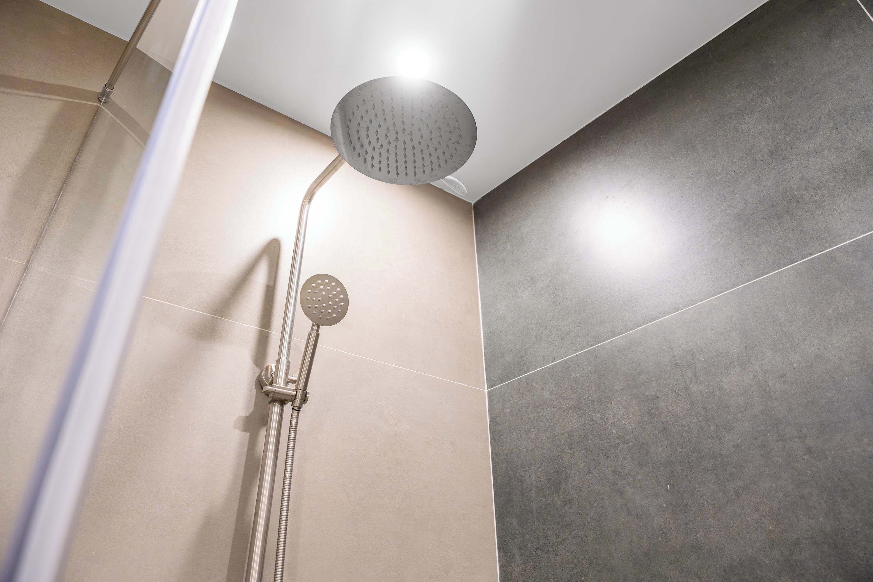 Eine Dusche mit Handbrause und Deckenbrause in einem modernen Badezimmer.