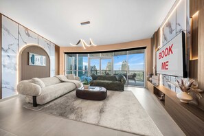 Ein modernes Wohnzimmer mit einer Couch, einem Couchtisch und einem großen Fernseher, der den Text 'BOOK ME' anzeigt.