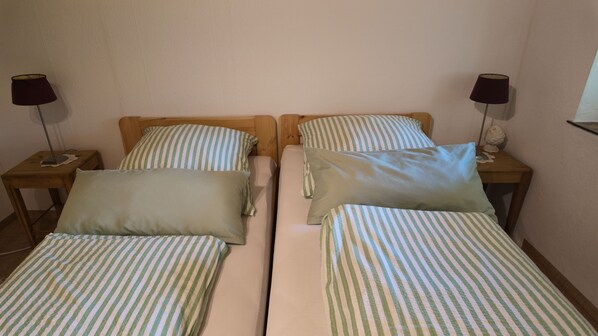 A double bed with a striped bedspread and pillows, a wooden headboard, and a nightstand with a lamp.