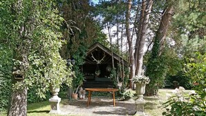 A rustic wooden structure with a bench in a lush garden setting.