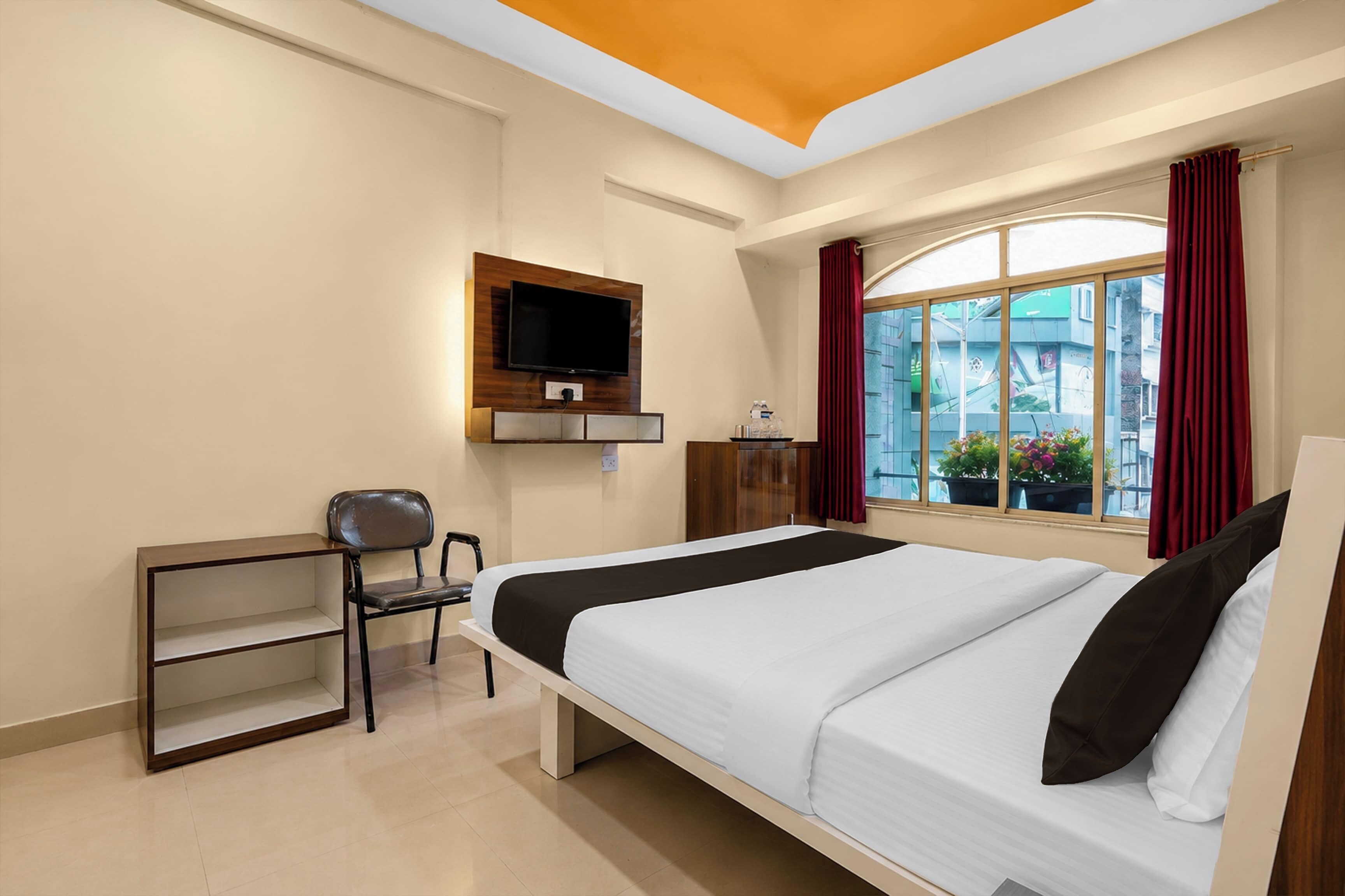 Habitación de hotel con cama, escritorio, silla, televisor montado en la pared y ventana con cortinas.