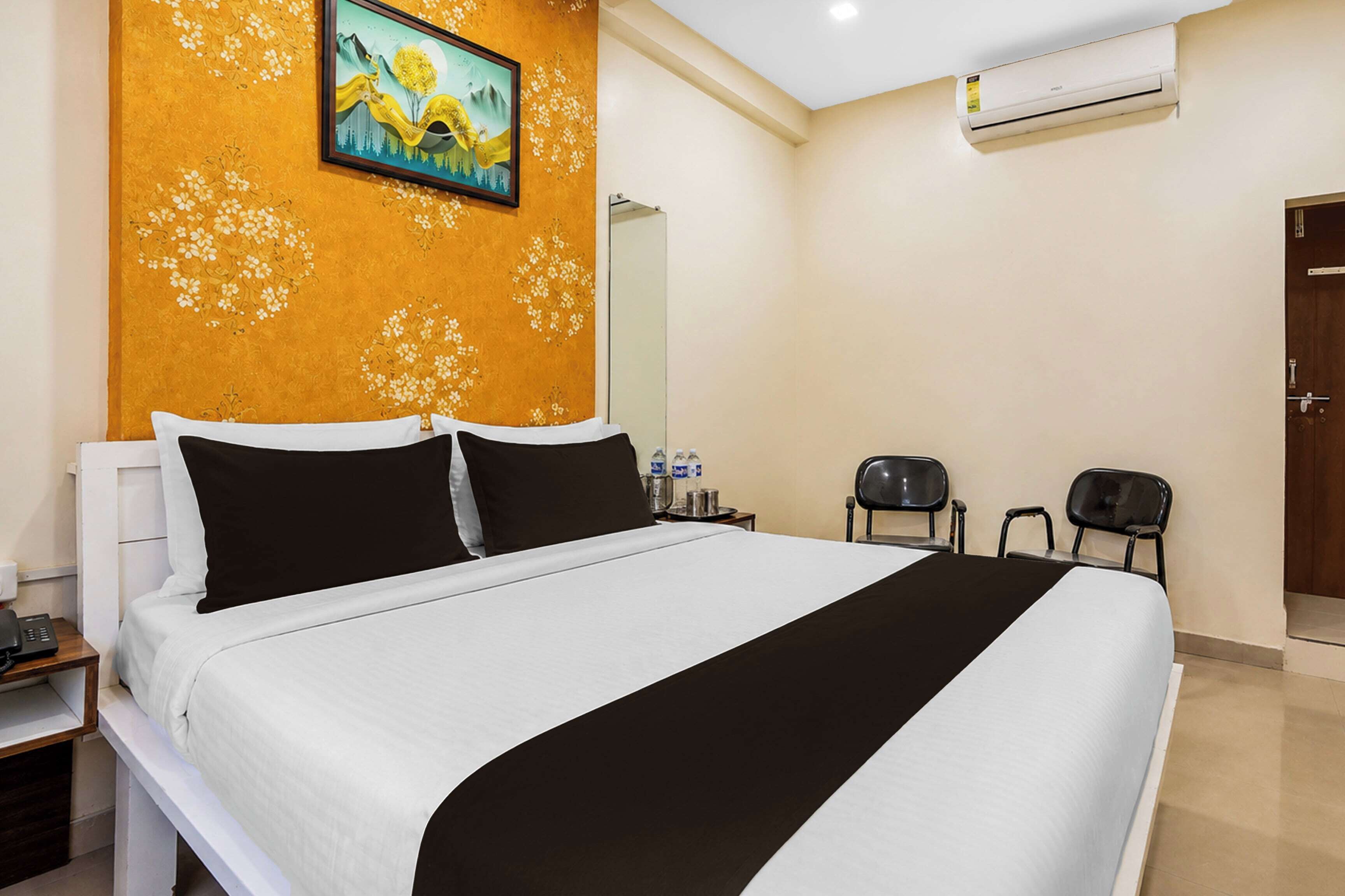 A hotel room with a large bed, a painting on the wall, an air conditioning unit, and a door.