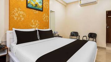 A hotel room with a large bed, a painting on the wall, an air conditioning unit, and a door.