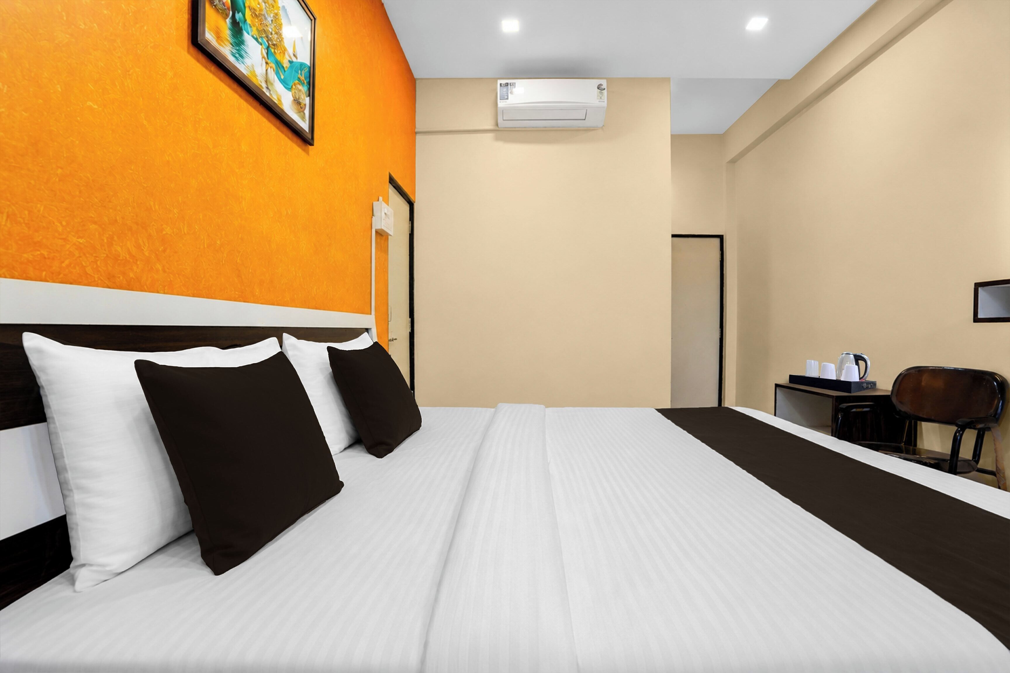 A hotel room with a large bed, an air conditioning unit, a desk with a chair, and a painting on the wall.