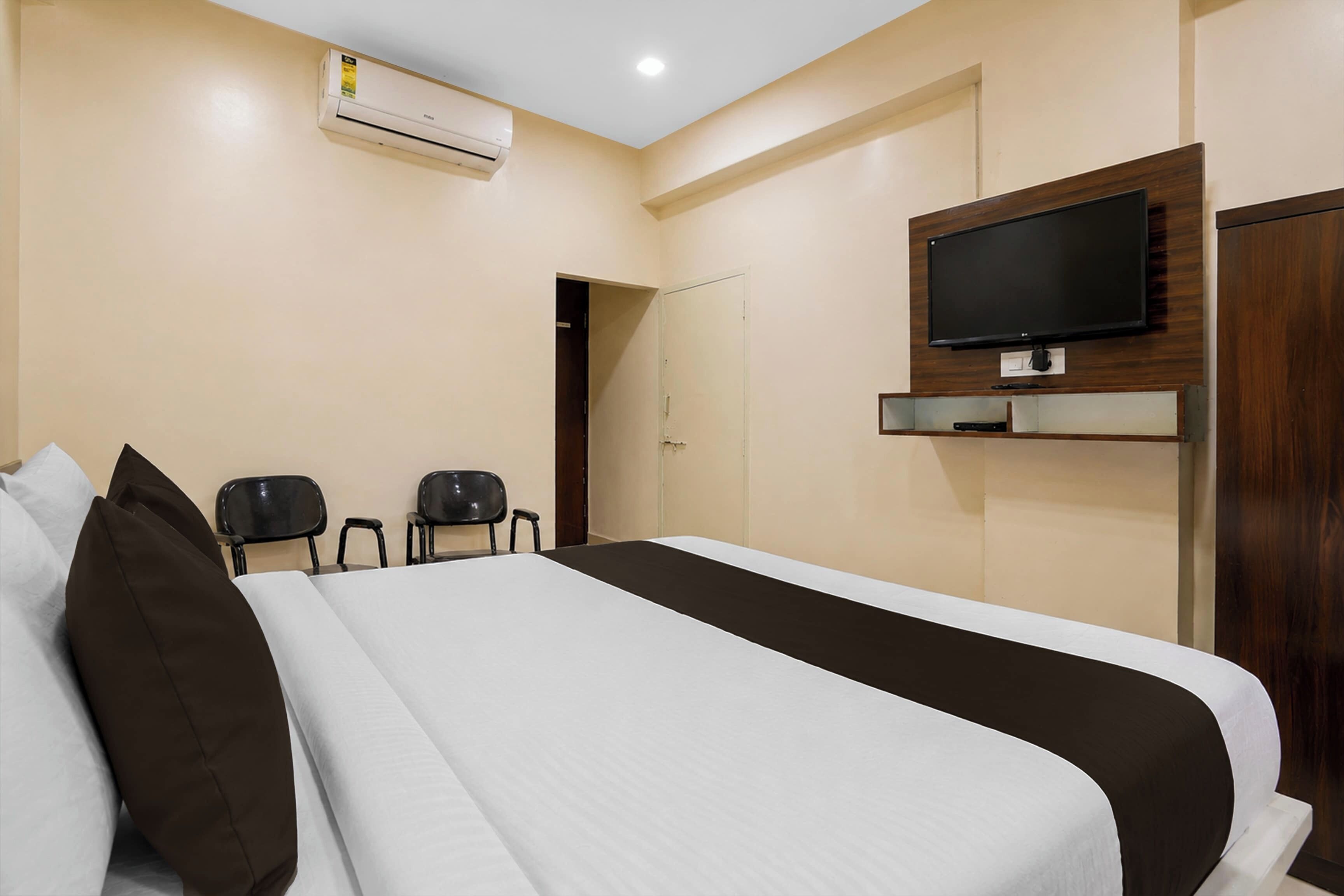 Ein Hotelzimmer mit einem Bett, einem an der Wand befestigten Fernseher und einer Tür zu einem weiteren Raum.