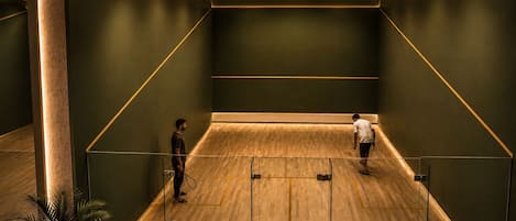 A squash court with wooden flooring, green walls, and a glass partition.
