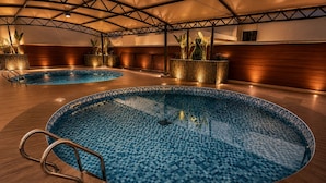 A large indoor swimming pool with a checkered tile pattern, surrounded by wooden flooring and plant arrangements. - Grand Unicorn Club (Islamabad)