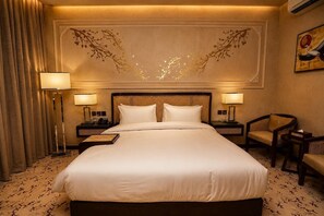 Ein Hotelzimmer mit einem großen Bett, zwei Nachttischen, einem Sessel und einer Wand mit dekorativem Design.