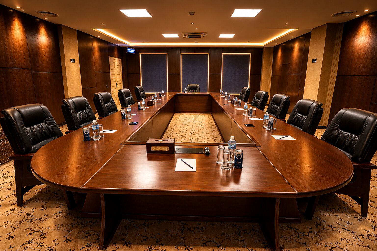 A conference room with a long table, leather chairs, water bottles, and a carpeted floor.