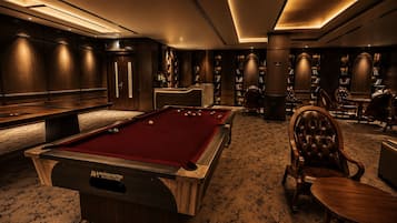 Una sala de billar con mesa de pool, estanterías y sillones de cuero.