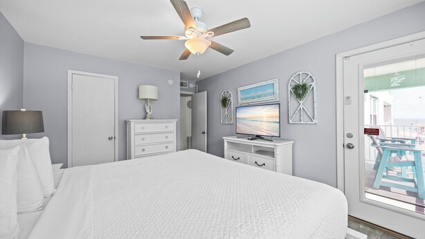 Une chambre à coucher avec un lit, un ventilateur de plafond, une télévision et une fenêtre donnant sur une piscine.