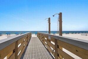 A wooden pier leading to a beach with blue umbrellas and lounge chairs. - 2BR Gulf-side condo w private beach access & heated pool (Gulf Shores)