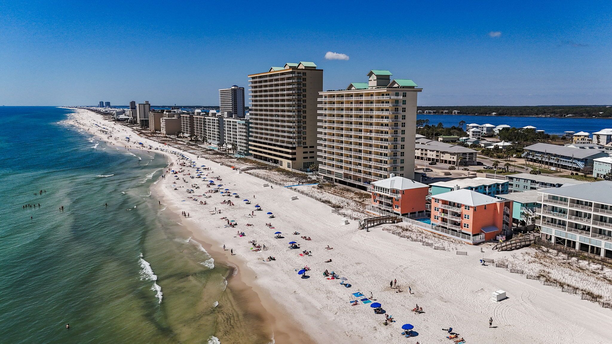 A coastal hotel with multiple floors, beachfront location, and a sandy beach with umbrellas.