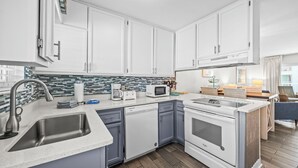 Une cuisine moderne avec des meubles blancs, un évier en acier inoxydable, un four à micro-ondes et une cuisinière.