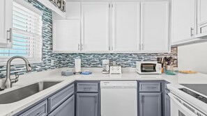 A modern kitchen with white cabinets, a stainless steel sink, a dishwasher, a microwave, and a toaster. - 2BR Gulf-side condo w private beach access & heated pool (Gulf Shores)