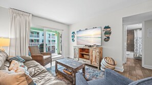 A living room with a sofa, armchair, coffee table, and a television. - 2BR Gulf-side condo w private beach access & heated pool (Gulf Shores)