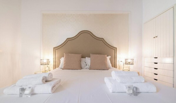 Una habitación de hotel con una cama grande, dos lámparas de noche, un armario y toallas dobladas con cuidado.