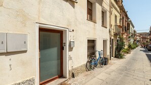 A narrow street with a building featuring a large glass door, a bicycle parked outside, and a clear sky. - Estay - The Corner House Cagliari Room 2 (Cagliari)