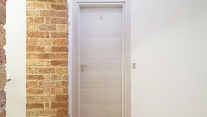 A closed door with a number '2' above it, adjacent to a brick wall. - Estay - The Corner House Cagliari Room 2 (Cagliari)