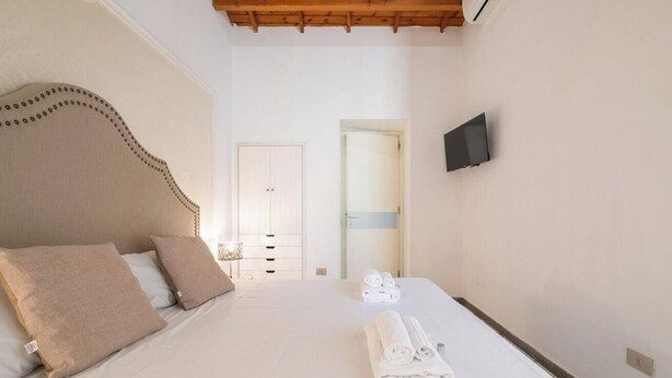 A bedroom with a bed, a television mounted on the wall, and a door leading to another room. - Estay - The Corner House Cagliari Room 2 (Cagliari)