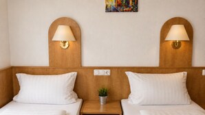 A hotel room with two beds, a wooden headboard, bedside lamps, a small plant, and a painting on the wall. - Dahlbrucher Hof (Hilchenbach)