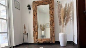 Una habitación con un espejo grande, un espejo con marco de piedra, una planta en maceta y un manto de piel sobre un piso de ladrillo.