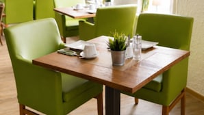 Un comedor con sillas tapizadas de verde y una mesa de madera, que incluye una planta en maceta y saleros y pimenteros.