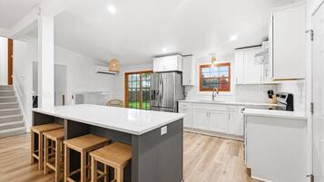Una cocina moderna con una isla central, taburetes de madera, armarios blancos y vistas al exterior.