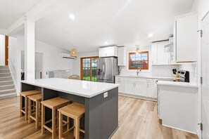 Una cocina moderna con una isla central, taburetes de madera, armarios blancos y vistas al exterior.