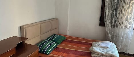 A bedroom with a bed, a wooden dresser, and a window with sheer curtains.