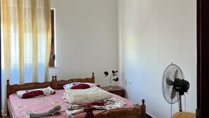 Une chambre à coucher avec un lit en bois, un ventilateur de plafond, un lustre et une fenêtre avec des rideaux.