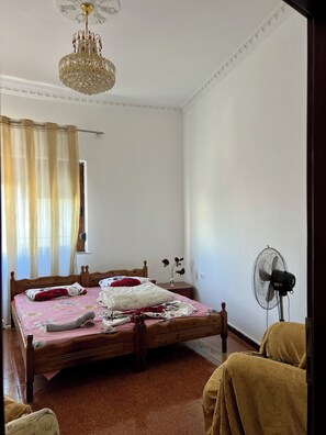 A bedroom with a wooden bed, a ceiling fan, a chandelier, and a window with curtains.