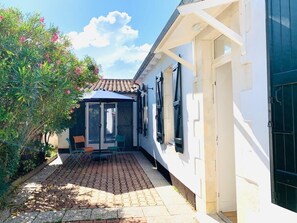 A courtyard with a paved walkway, a glass door entrance, and a small seating area with chairs. - Village house 300 meters from the beach.  Pets are allowed. (Sainte-Marie-de-Ré)