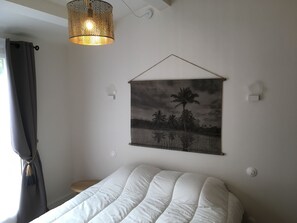 A bedroom with a bed, a hanging light fixture, a wall-mounted picture, and a window with curtains. - Village house 300 meters from the beach.  Pets are allowed. (Sainte-Marie-de-Ré)