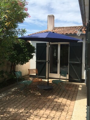 A patio area with a blue umbrella, outdoor seating, and a view of a building with a tiled roof. - Village house 300 meters from the beach.  Pets are allowed. (Sainte-Marie-de-Ré)