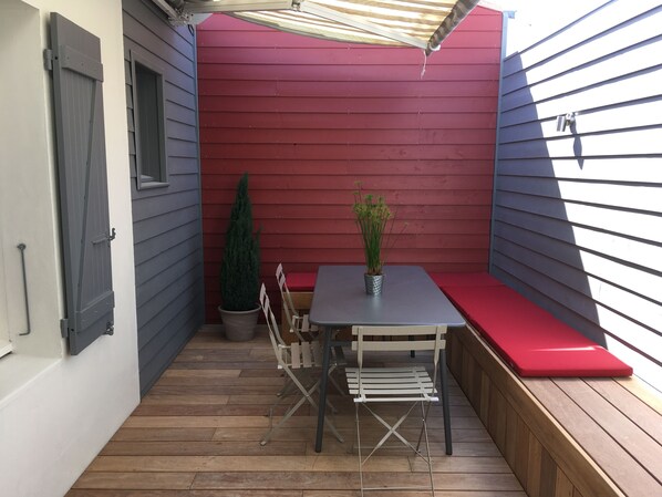 En terrasse med et bord, stole, en bænk og en potteplante.