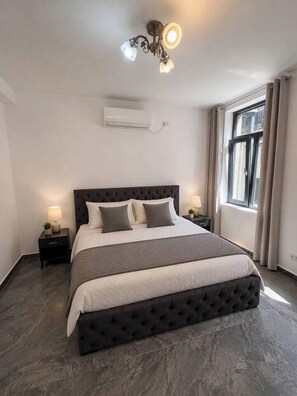 Ein Schlafzimmer mit einem großen Bett, Nachttischen, einer Deckenleuchte, einer Klimaanlage und einem Fenster mit Vorhängen.