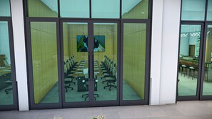 Un salón de conferencias con una larga mesa y sillas, una pantalla de televisión y un panel de vidrio.