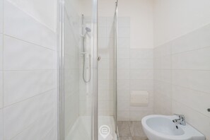 Un baño con ducha de mampara de vidrio, lavamanos blanco y paredes con azulejos.