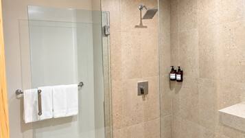 Une douche fermée par des parois en verre, dotée d’un pommeau de douche à main, d’un porte-serviettes avec deux serviettes et de deux bouteilles de shampoing fixées au mur.