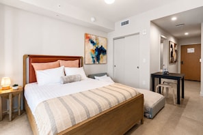 A hotel room with a bed, bedside table, lamp, and a desk with a chair. - The Crosby (Miami)