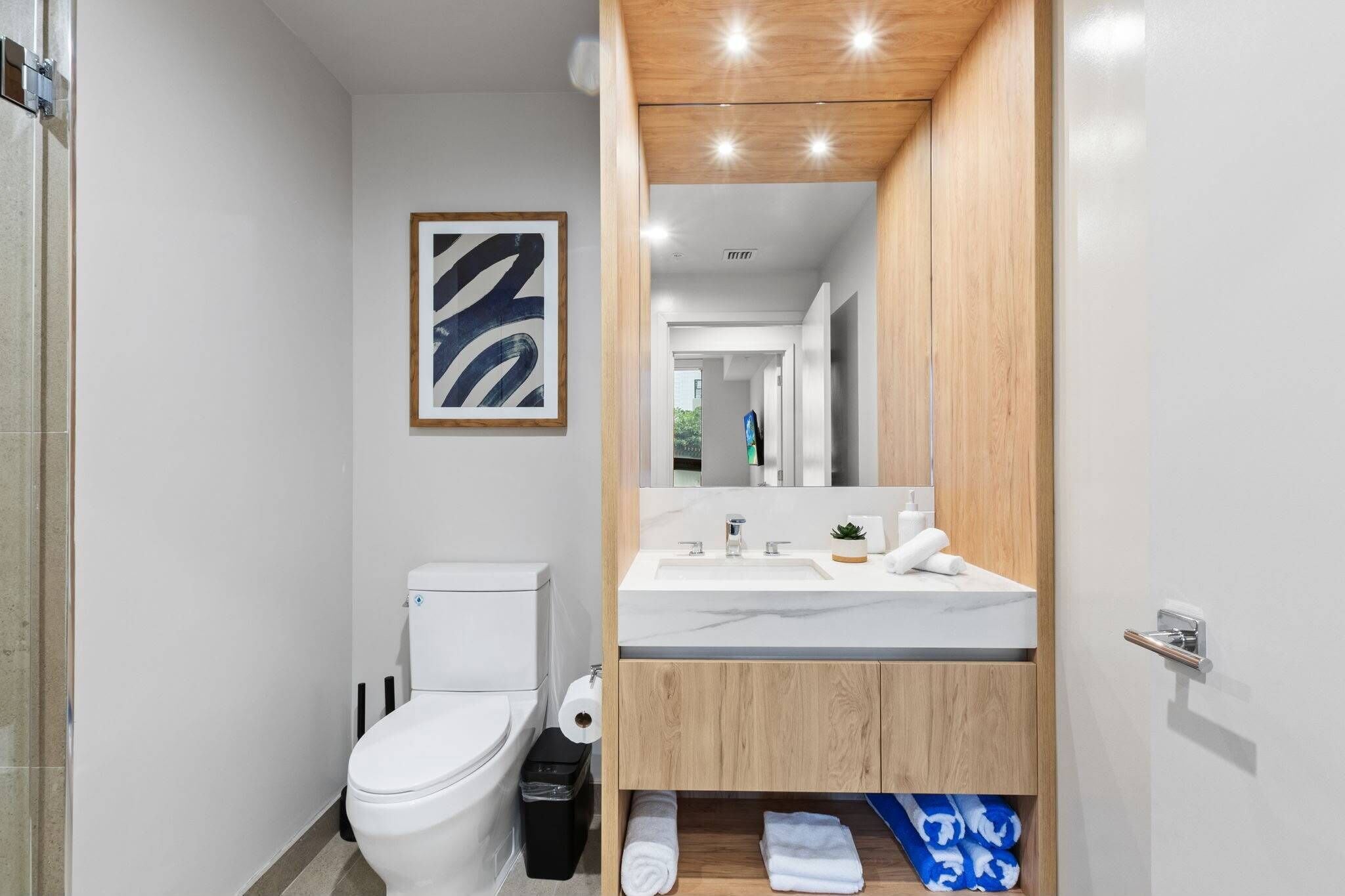 Une salle de bain moderne comprenant des toilettes, un lavabo, un miroir et une œuvre d’art abstraite encadrée accrochée au mur.