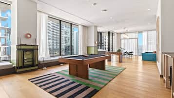 Een moderne woonkamer met een pooltafel, grote ramen en uitzicht op een stadsbeeld.