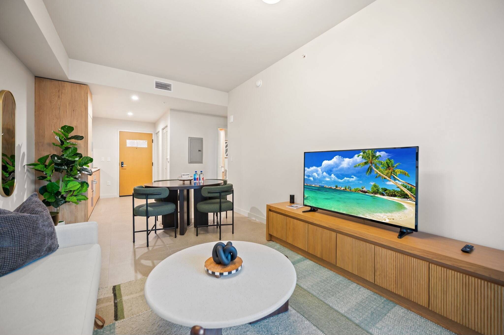 A modern living room with a flat-screen TV, a dining area with chairs, a sofa, and a coffee table.