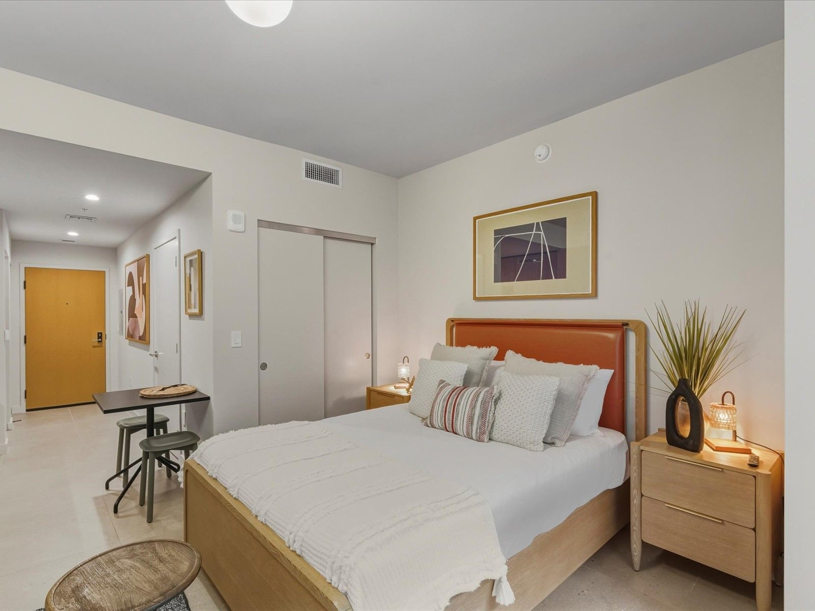 A bedroom with a bed, nightstand, and a desk with a chair.