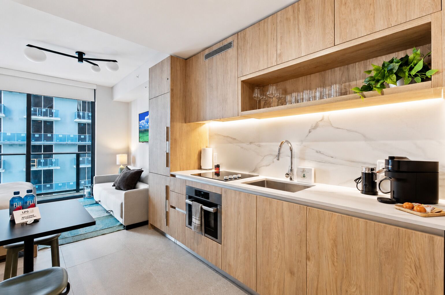 A modern kitchen with wooden cabinets, a marble countertop, a built-in oven, and a coffee machine.