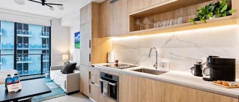 A modern kitchen with wooden cabinets, a marble countertop, a built-in oven, and a coffee machine.