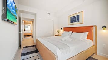 Een hotelkamer met een bed, een televisie, een ingelijst schilderij en een badkamer door een open deur zichtbaar.