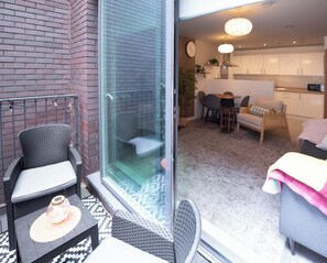 Eine moderne Wohnung mit Glastür, die auf einen Balkon führt, einem Küchenbereich und einer Sitzecke mit Sofa und Sesseln.